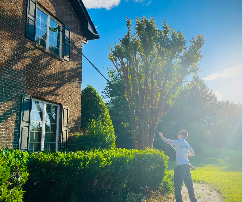 Jackson cleaning second-story brick home windows with a water-fed pole on a sunny day