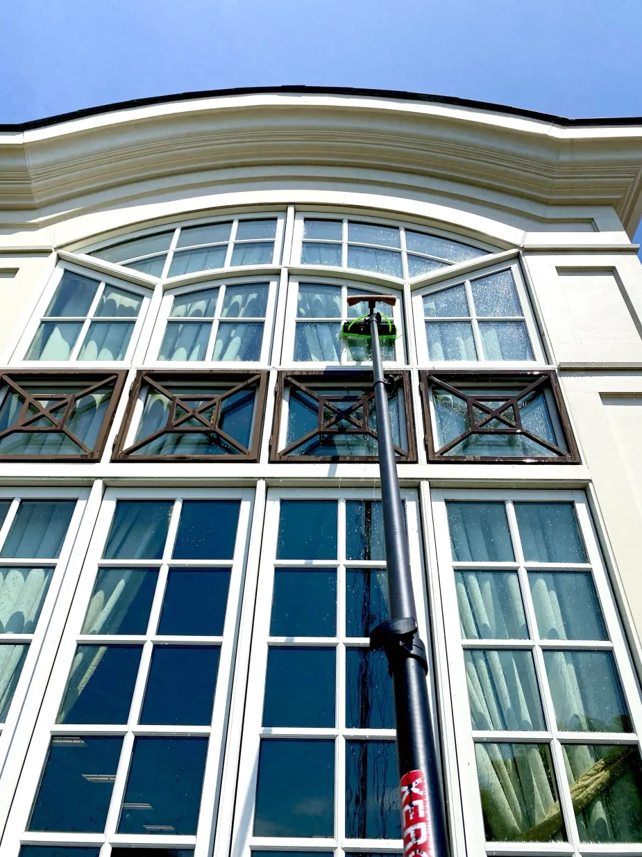 Technician using a water-fed pole to clean tall multi-pane exterior windows